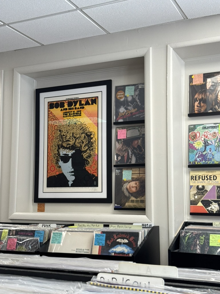 Record bins organized by genre under a Bob Dylan concert poster