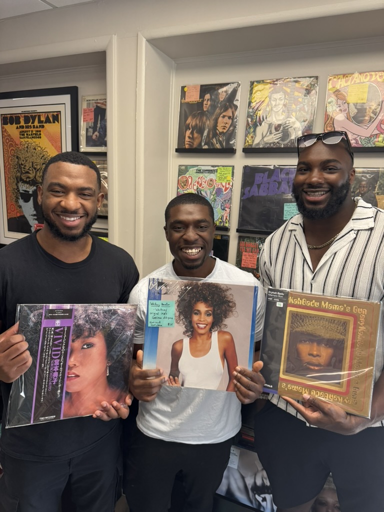 Three customers in the shop holding records they found, including Whitney Houston and Erykah Badu
